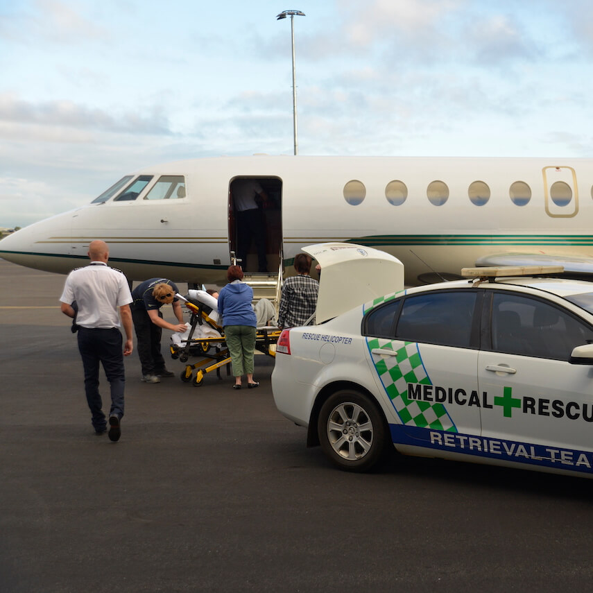A patient on a stretcher next to an air ambulance jet on a runway